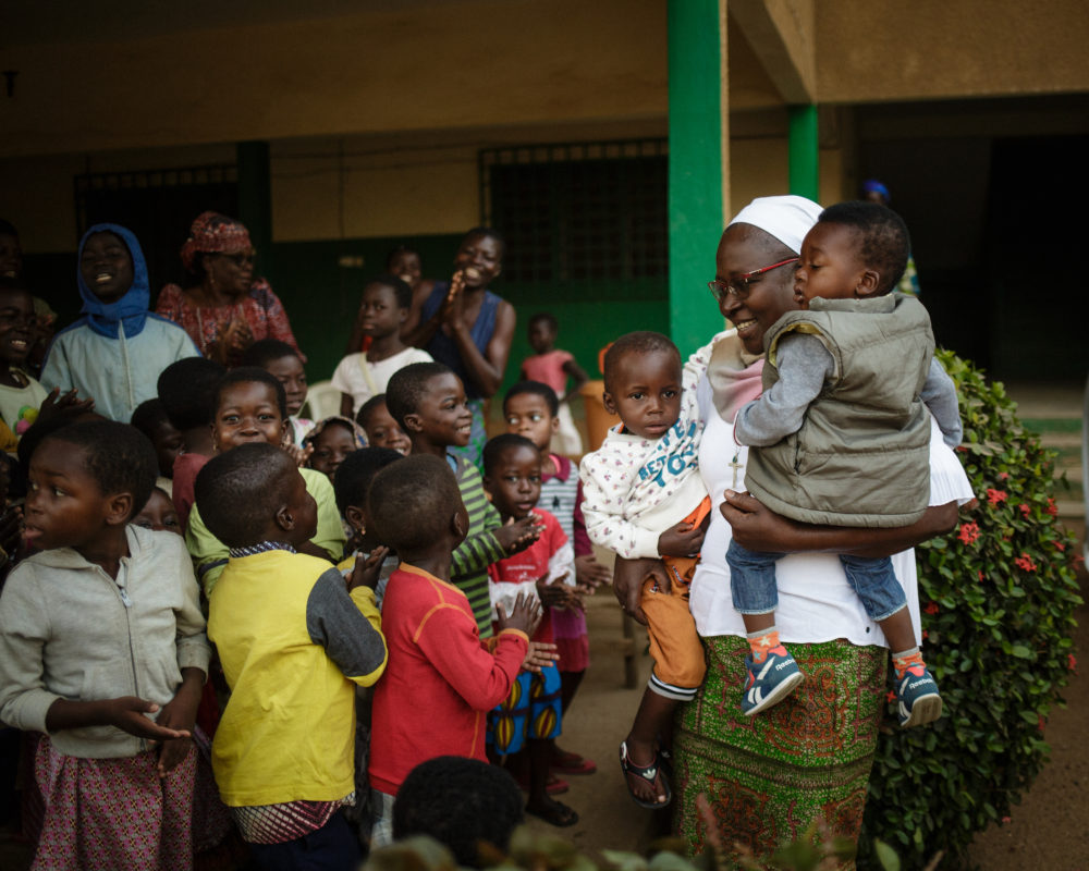 woman surrounded by children, while holding two children